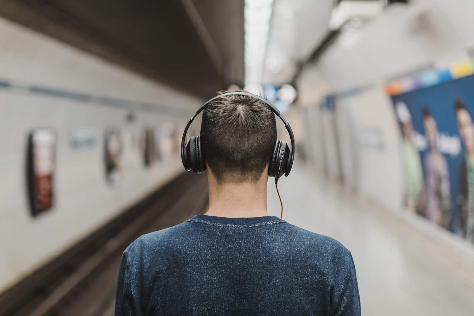 Man wearing headphones at a train station listening to a podcast.
