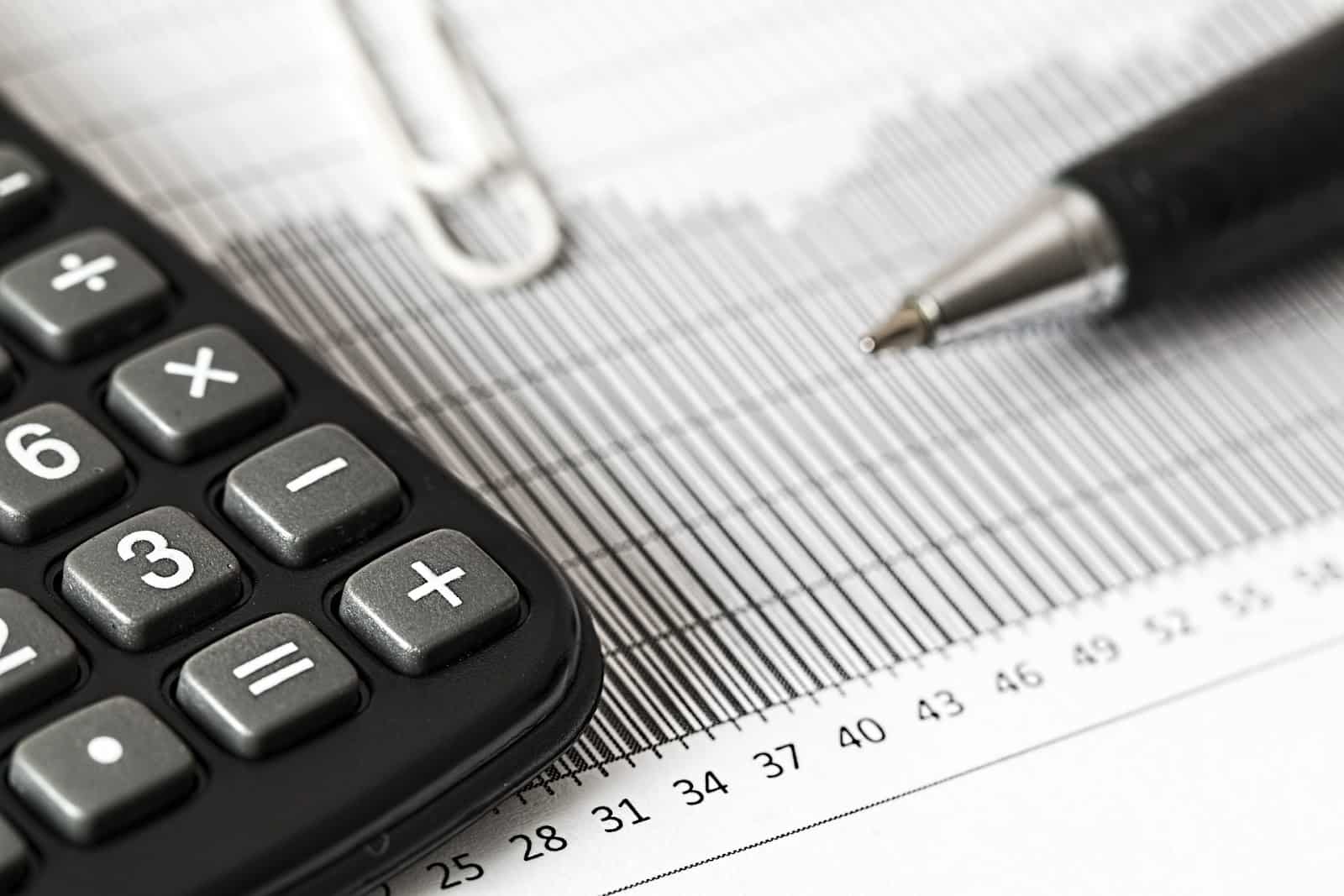 A calculator, pen, and graph being used by someone to calculate entrepreneurial investment opportunities.